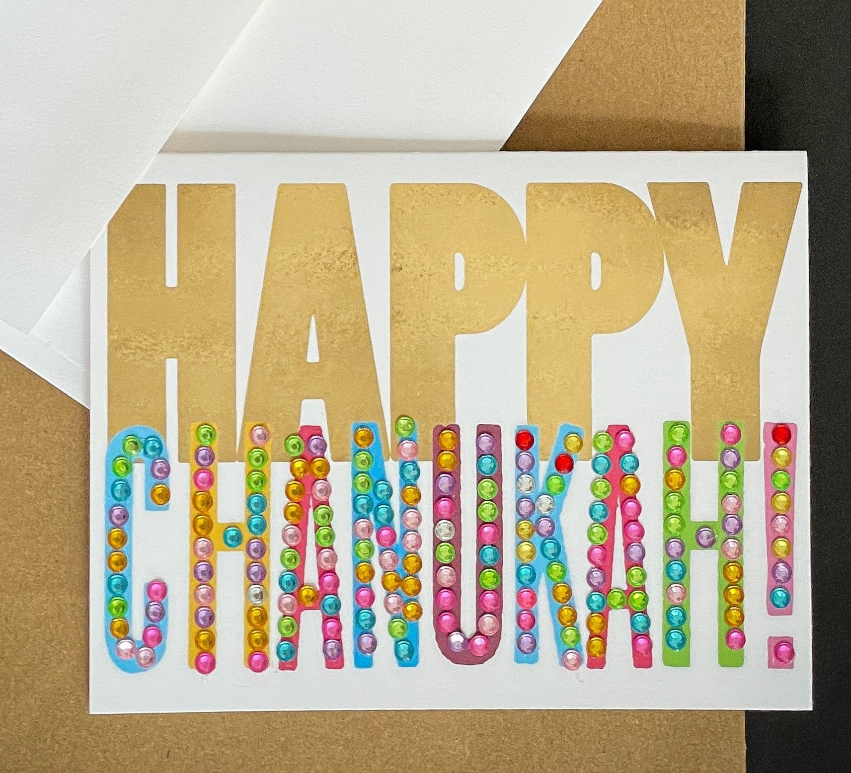 this is a note card on a craft paper gift bag with a white envelope and a black marker , the card has Happy Chanukah written on it