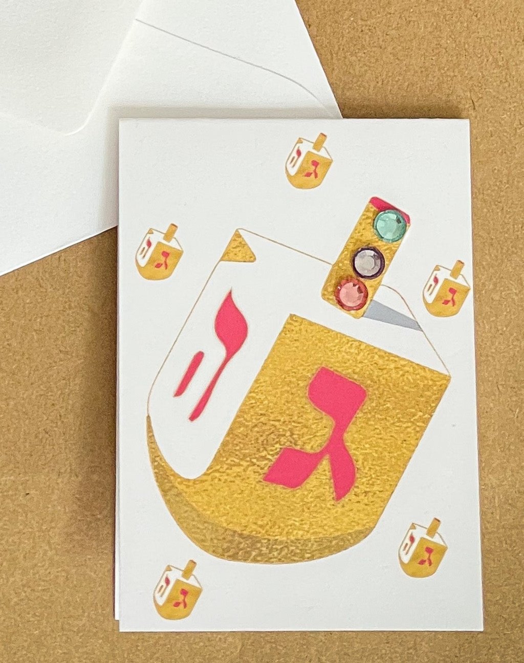 this is a mini note card on a craft paper gift bag with a white envelope and a black marker , the card has a gold dreidel