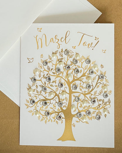 this is a note card on a craft paper gift bag with a white envelope and a black marker , the card says Mazel Tov and there is a gold tree of life