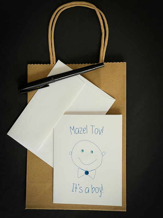 this is a note card on a craft paper gift bag with a white envelope and a black marker , the card says Mazel Tov! It’s A Boy! With a cute drawing of a baby boy