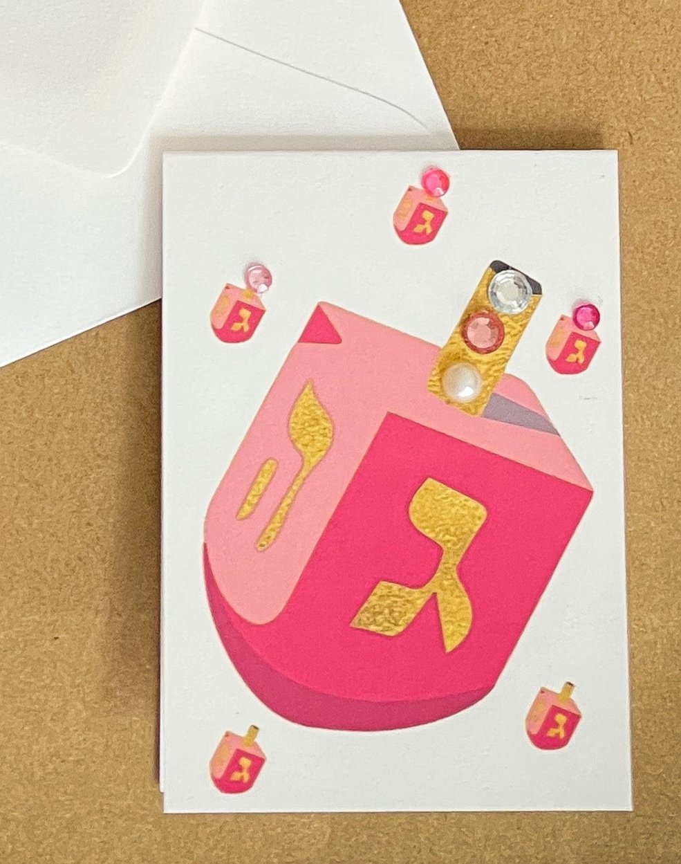 this is a mini note card on a craft paper gift bag with a white envelope and a black marker , the card has a pink dreidel 