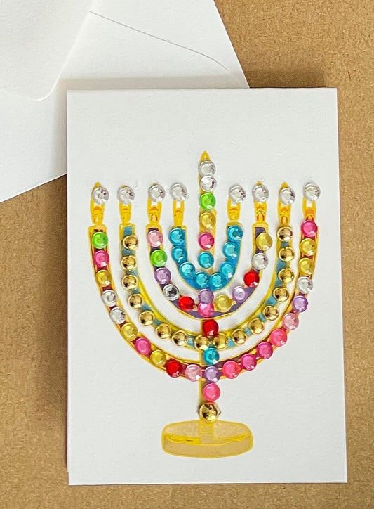 this is a mini note card on a craft paper gift bag with a white envelope and a black marker , the card has a decorated menorah