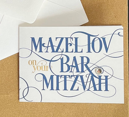 this is a mini note card on a craft paper gift bag with a white envelope and a black marker , the card says Mazel Tov on your bar mitzvah in blue