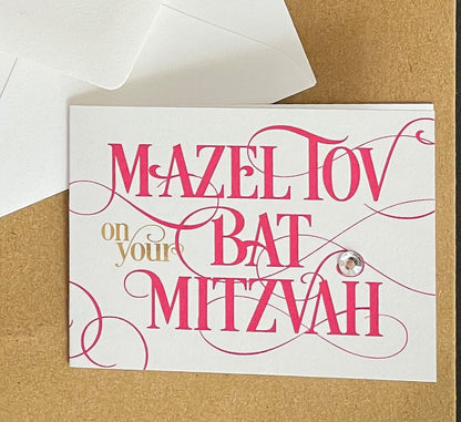 this is a mini note card on a craft paper gift bag with a white envelope and a black marker , the card says Mazel Tov on your bat mitzvah in hot pink