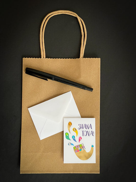 this is a mini note card on a craft paper gift bag with a white envelope and a black marker , the card says Shana Tova in English with a shofar