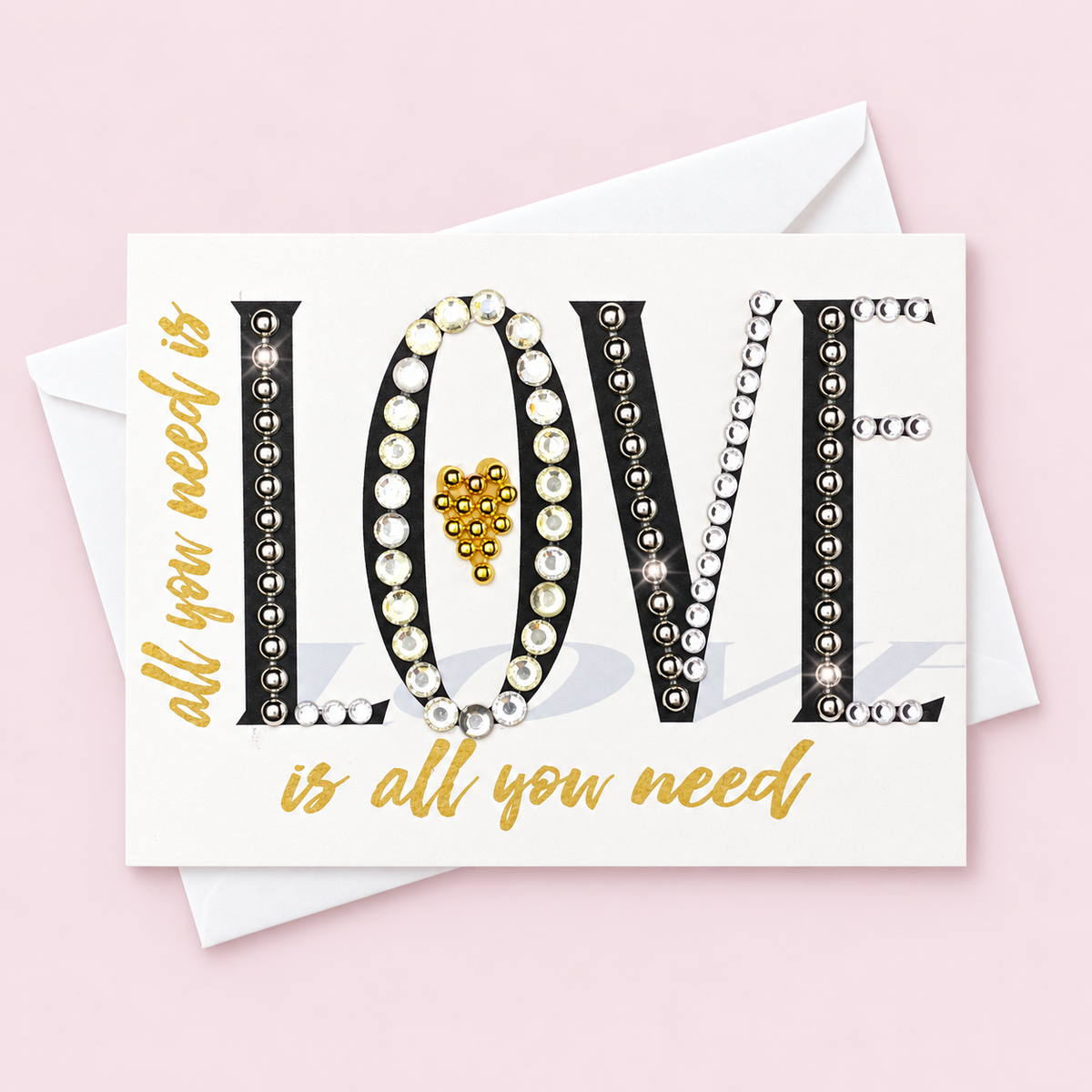 All You Need Is Love Black, Gold + Crystal with white envelope on a pale pink background