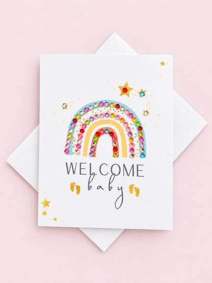 Welcome Baby Rainbow Pastel greeting card with its original design, shown with a white envelope on a pale pink background