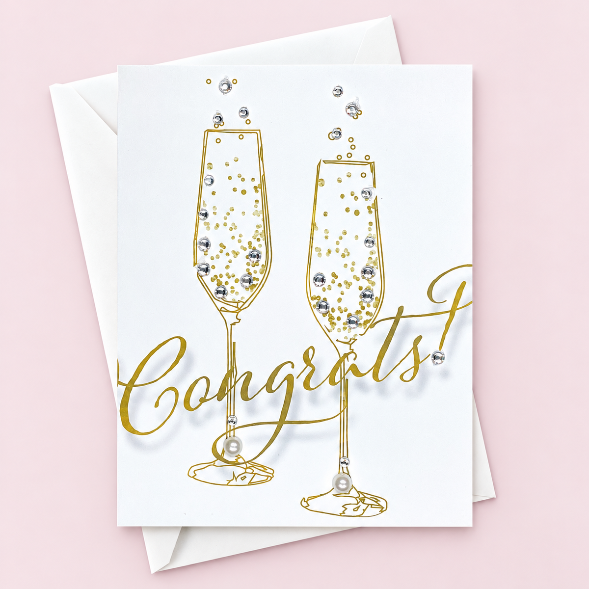 Congratulations champagne glasses greeting card with hand-applied sparkling details with a white envelope on pale pink