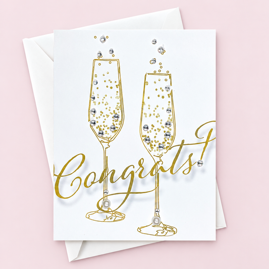Congratulations champagne glasses greeting card with hand-applied sparkling details with a white envelope on pale pink