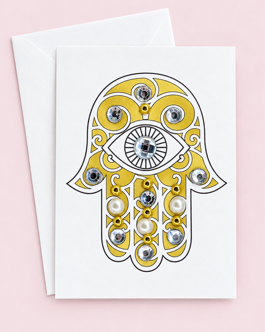 Mini Gold Hamsa Eye greeting card with its original design, shown with a white envelope on a pale pink background