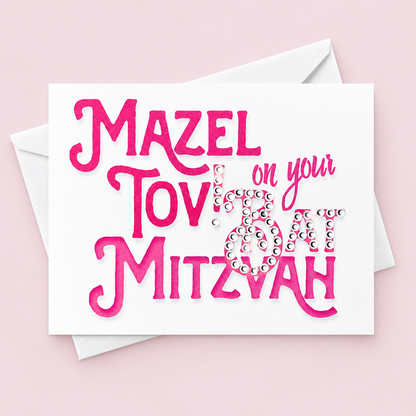 Mazel Tov on your Bat Mitzvah card with pink lettering and crystal embellishments, with a white envelope on a pale pink background.
