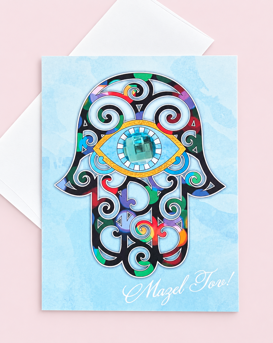 Mazel Tov Hamsa greeting card with its original design, shown with a white envelope on a pale pink background