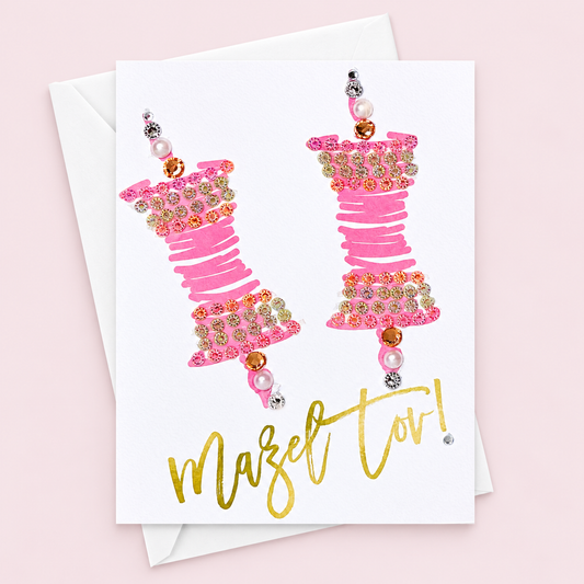 Mazel tov pink scrolls with a white envelope on a pale pink background